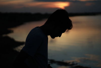 Side view of man standing on beach against sky during sunset