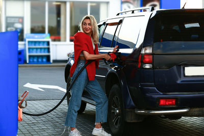 Young woman refueling her car at a gas station. attractive blonde female student. blurred selective 