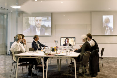 Male and female professionals discussing in global business meeting seen through glass wall at workplace