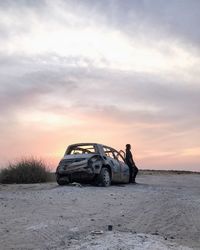 Abandoned car on snow against sky during sunset