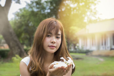 Close-up portrait of young woman holding white flowers in yard