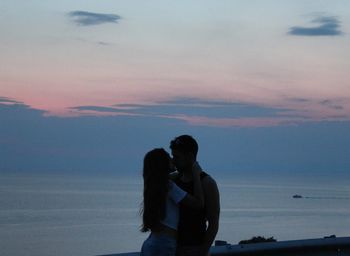 Silhouette couple in sea against sky during sunset