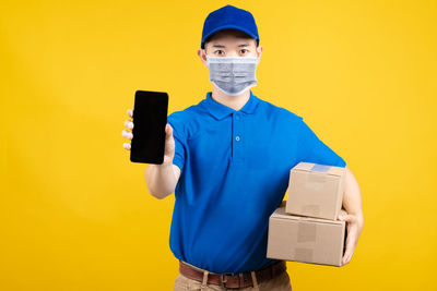 Portrait of man holding camera against yellow background