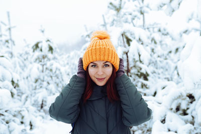 Cheerful girl in warm clothes playing with snow outdoors near the beautiful forest