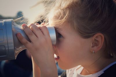 Close-up of girl looking through coin-operated binocular