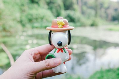 Cropped hand holding figurine against lake