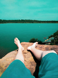 Low section of man relaxing by sea against sky