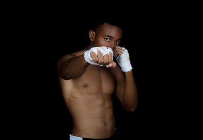 Portrait of shirtless muscular man with wrapped hands against black background