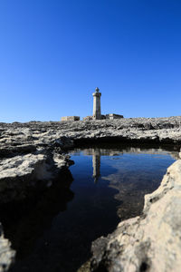 Lighthouse by building against clear blue sky