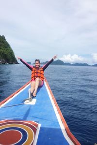 Portrait of smiling young woman with arms raised sitting on boat sailing on sea