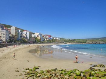 People on beach against clear blue sky