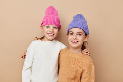 Portrait of smiling sisters wearing knit hat against beige background