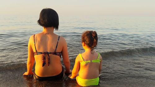 Rear view of siblings sitting at beach during sunset