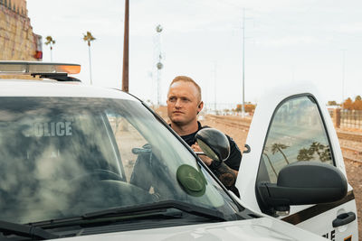 Horizontal image of white male caucasian police officer standing in the door opening of his trooper 