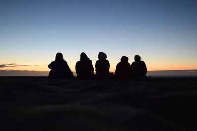 Silhouette people sitting at beach against sky during sunset