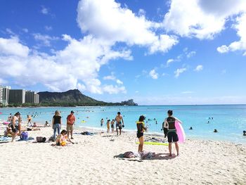 People at beach against cloudy sky during sunny day