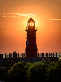 Silhouette lighthouse by sea against orange sky