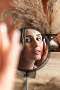 A young woman in front of a mirror applies a moisturizer on her face. beauty portrait