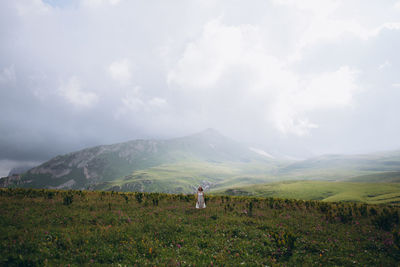 Woman sanding on field against mountains and sky