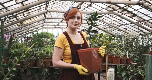 Portrait of smiling woman holding potted plant in greenhouse
