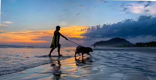 Woman with dog on beach against sky during sunset