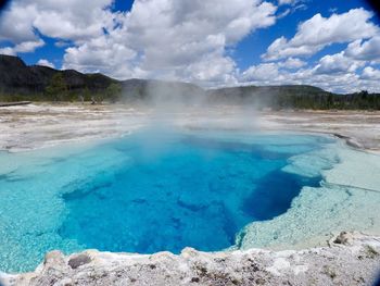 Smoke emitting from sapphire pool at yellowstone national park against cloudy sky