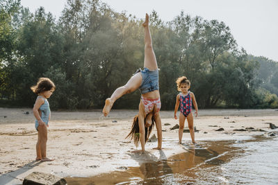Daughters watching mother cartwheeling at beach