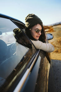 Portrait of young woman in car against sky