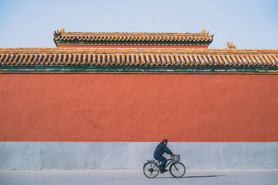 Man riding bicycle on building against sky