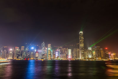 Illuminated buildings by river against sky at night