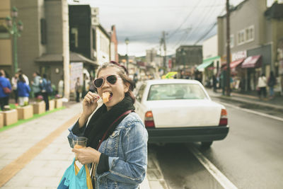 Portrait of woman eating food on street in city