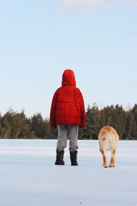 Rear view of boy with dog standing on snow covered field
