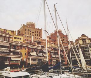 Sailboats moored on harbor against sky in city