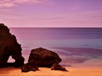 Rocks on sea shore against sky during sunset