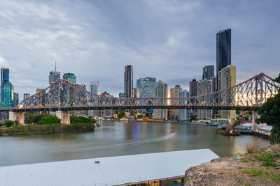 Bridge over river by buildings against sky in city