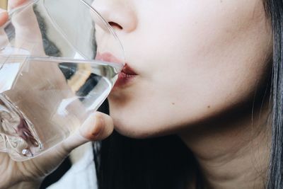 Close-up midsection of young woman drinking water at home