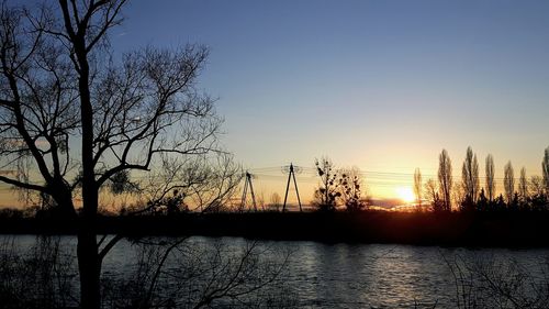 Silhouette bare trees by lake against sky during sunset