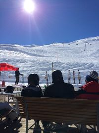 Rear view of friends sitting on bench in front of snowcapped mountains