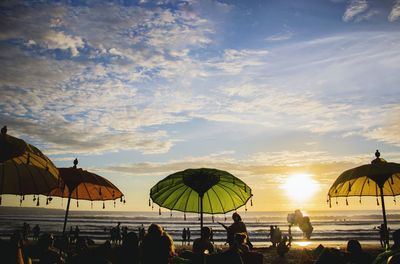 People relaxing at beach against sky during sunset