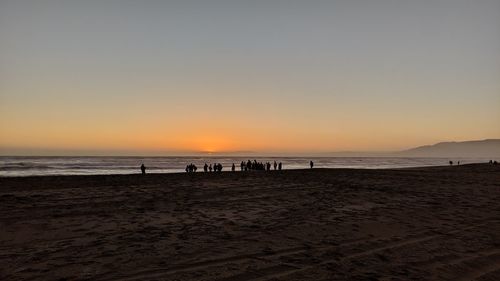 Silhouette people on beach against clear sky during sunset