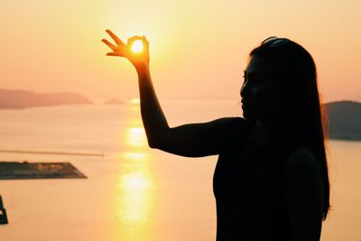 Silhouette woman standing by sea against sky during sunset