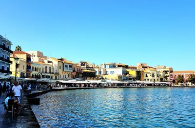 Buildings by river against clear blue sky