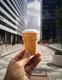 Close-up of hand holding ice cream cone against buildings