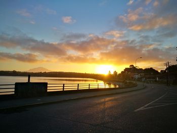 Road by silhouette city against sky during sunset