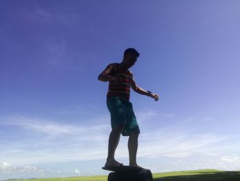 Full length rear view of man standing against blue sky