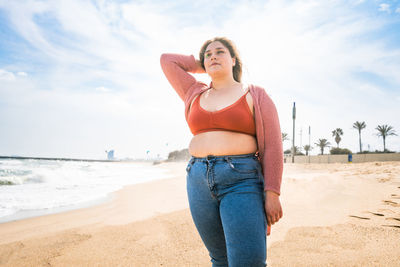 Young woman standing at beach against cloudy sky