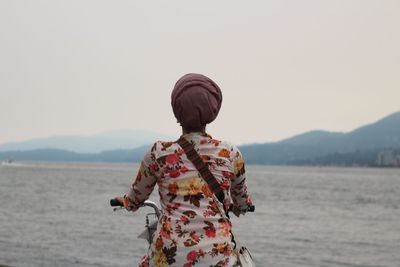 Rear view of woman standing by sea against clear sky