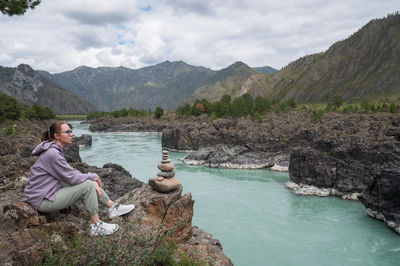 Rear view of woman sitting on rock by sea against mountain