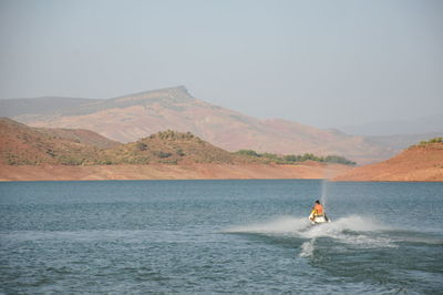 Rear view of man riding motorboat on sea against clear sky