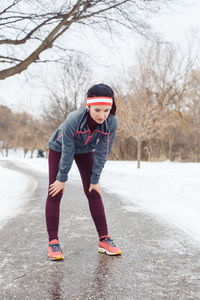 Full length of tired woman standing on road during winter